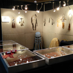 Display booth with walls, lights and tables showing jewelry pieces made by Artist Nelda Schrupp