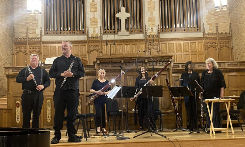 Six members of the New York Kammermusiker standing at the front of First Presbyterian Church in Fargo, wearing all black, holding double-reed instruments with music standing in front of them